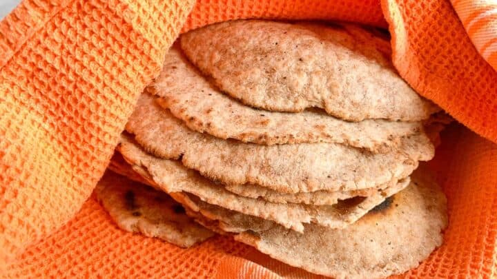 Whole Wheat Sourdough Tortillas wrapped in orange kitchen towel to keep warm.