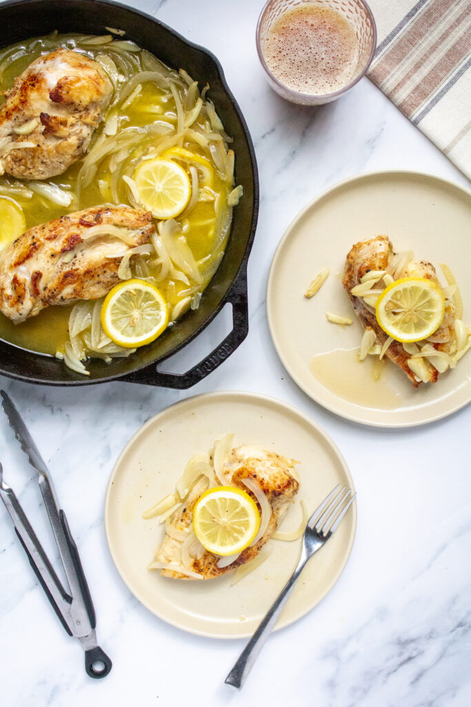 chicken topped with onions, garlic, and lemon on two plates