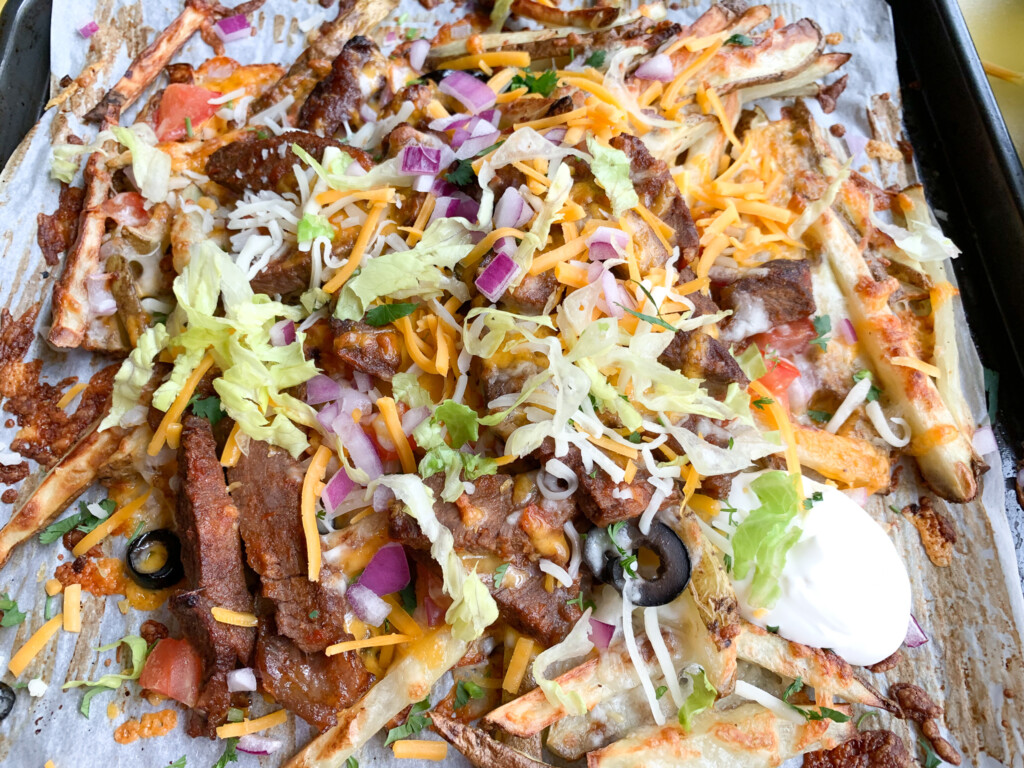 top view of carne asada fries with toppings such as steak, sour cream, lettuce, and olives with cheese