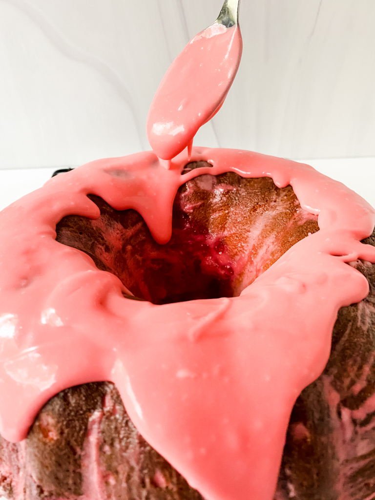 spoon drizzling pink glaze over strawberry pound cake