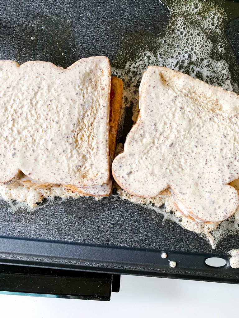 French-toast-peanut-butter-and-jelly-sandwich cooking on griddle with butter